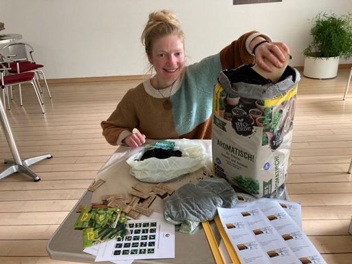 Junge Person hantiert mit Erde und Samen an einem Tisch.