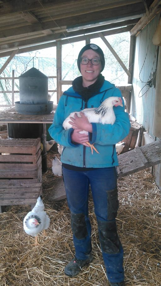 Junge Person hält im Stall Huhn in den Armen.