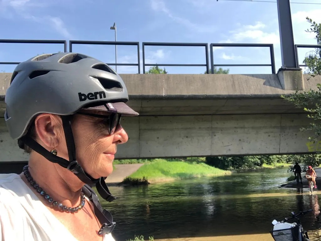 Person mit Helm auf Fahrrad vor Brücke.