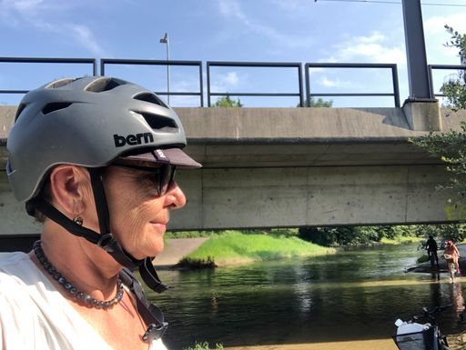 Person mit Helm auf Fahrrad vor Brücke.