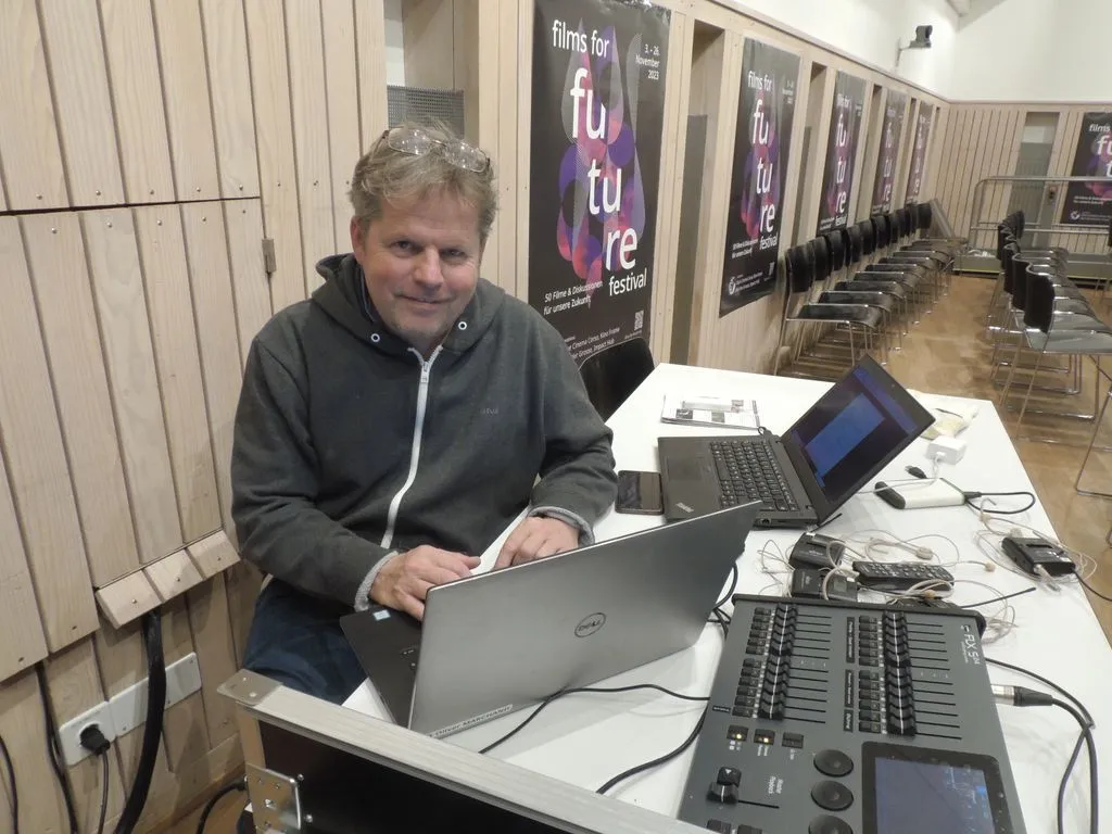 Person sitzt an Tisch mit Computer, Filmposter an den Wänden.