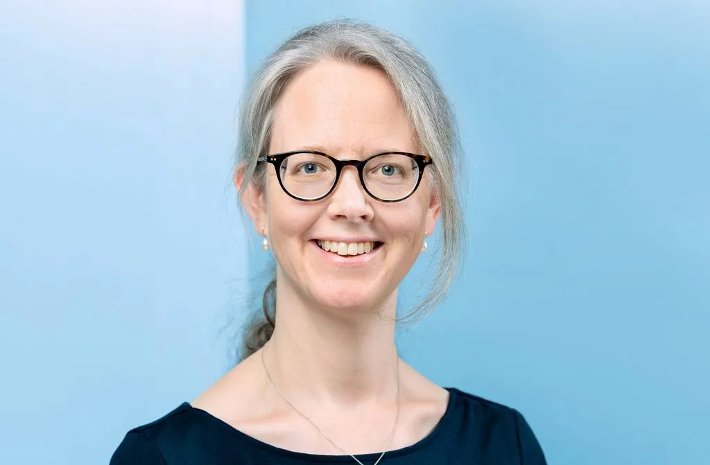 Person mit langen Haaren und Brille vor blauer Wand.
