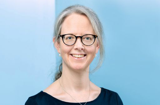 Person mit langen Haaren und Brille vor blauer Wand.