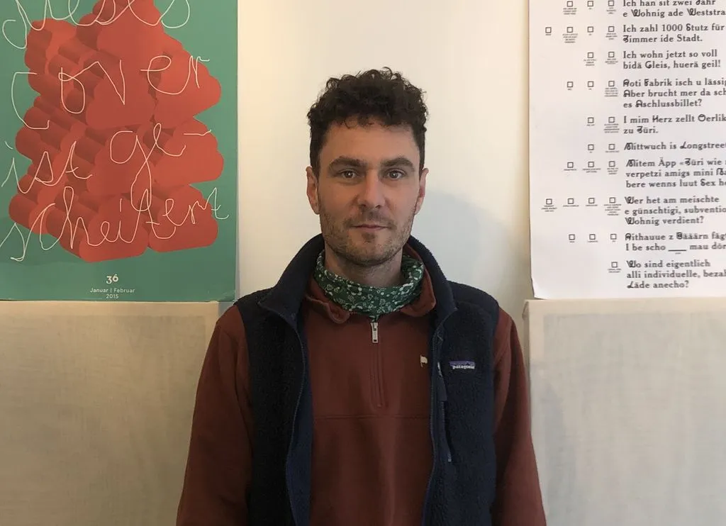 Person mit Halstuch steht vor Wand mit Postern.