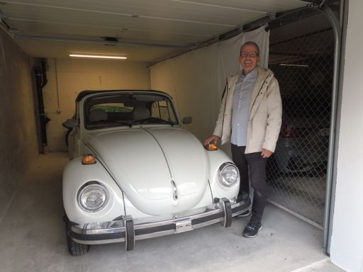 Lachende Person steht neben einem Oldtimer-Auto.