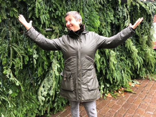 Lachende Person steht mit erhobenen Händen vor Pflanzen.