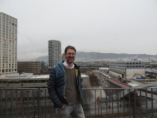 Person steht auf Terrasse vor einer Baustelle in einer Stadt.