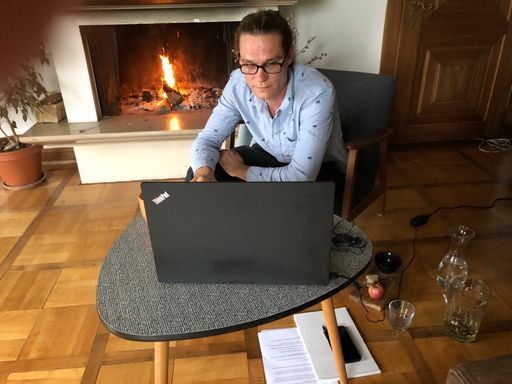 Junger Mann sitzt vor Cheminee am Laptop.
