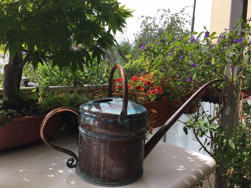 Eine kleine kunstvolle Giesskanne auf einem Balkon mit Blumen.