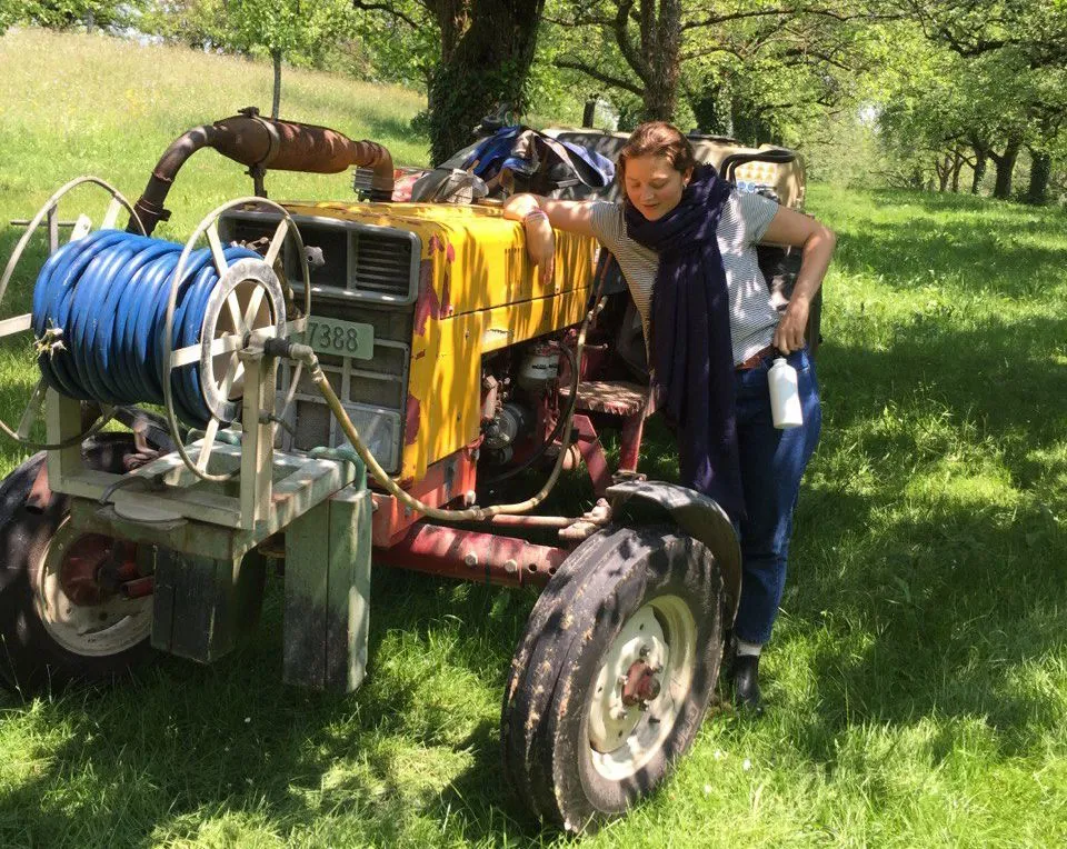 Junge Frau steht neben kleinem Traktor auf Wiese