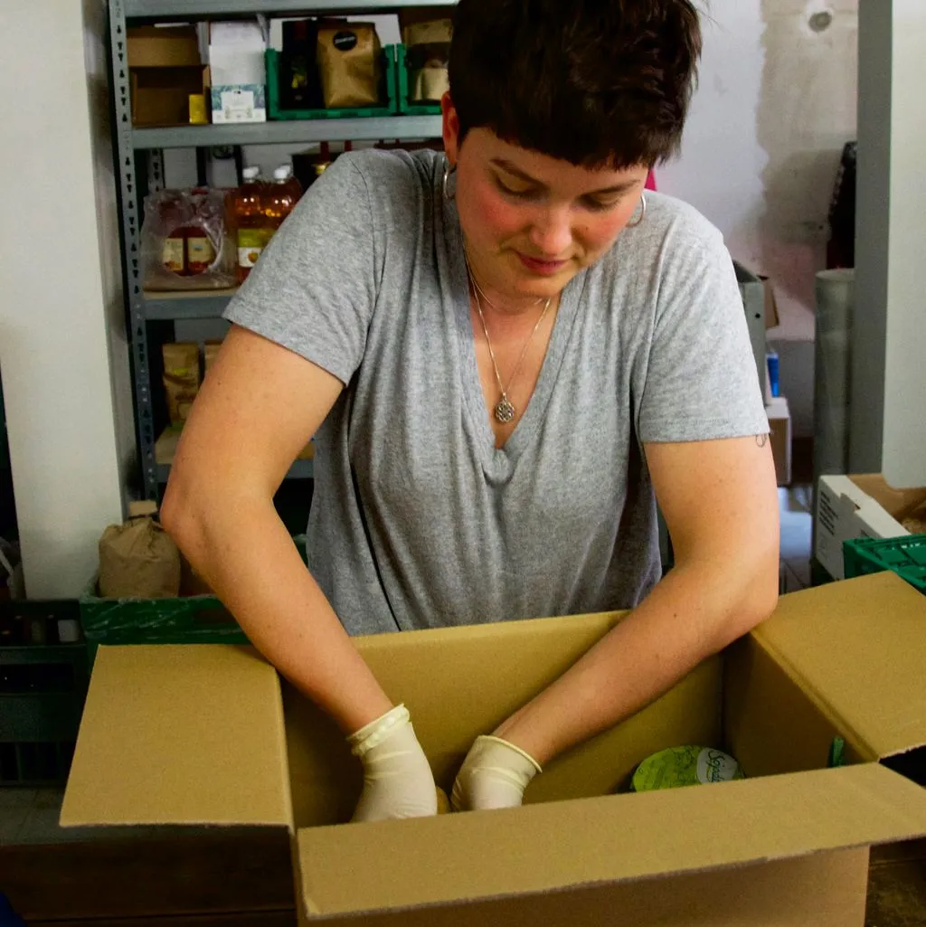 Junge Person packt Lebensmittel in eine Kartonkiste.