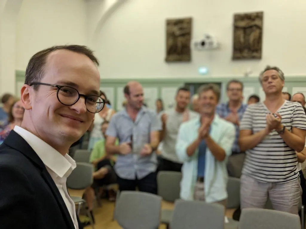 Mann mit Anzug steht vor seinem klatschenden Team.