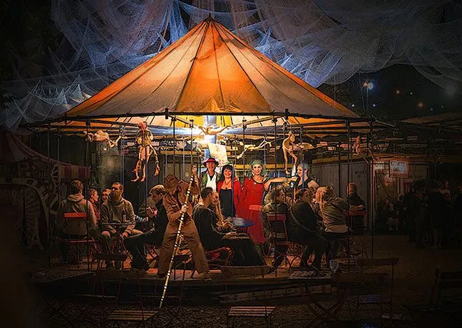 Ein hellbeleuchtetes Karrussell mit Tischen und Menschen.