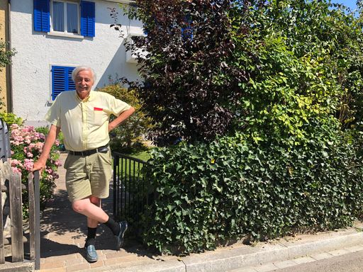 Pensionär steht in kurzen Hosen im Vorgarten.