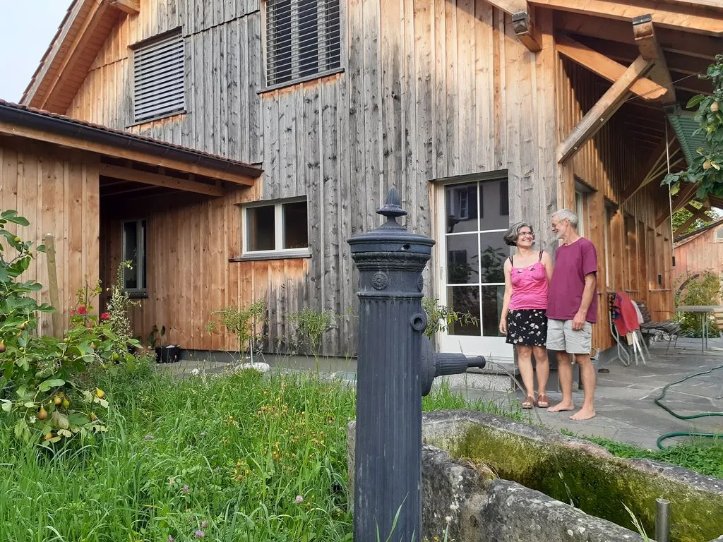 Mann und Frau stehen in kurzen Hosen vor Holzhaus