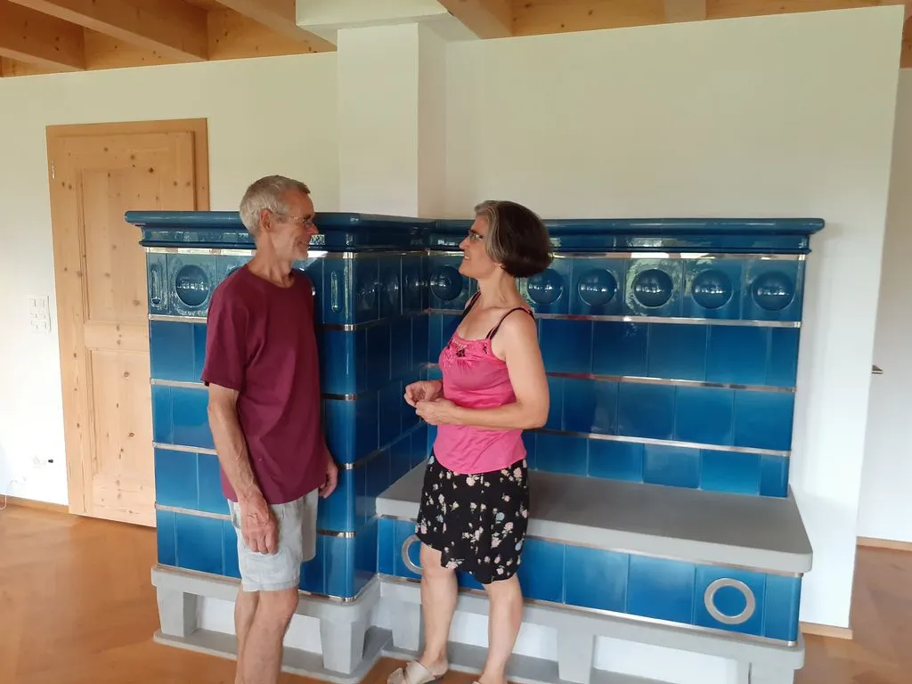 Frau und Mann stehen vor blauem Kachelofen.