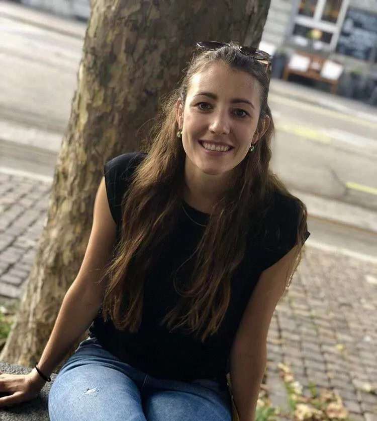 Junge Frau sitzt auf Stein vor Baum in der Stadt.