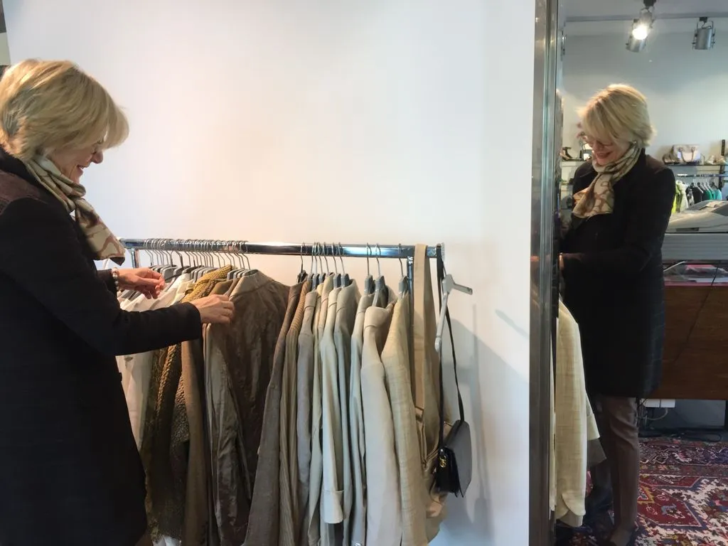 Eine ältere Frau geht Kleider an einem Kleiderständer durch