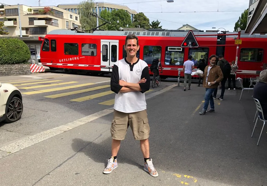 Lachender Mann mit verschränkten Armen vor Stadtbahn.