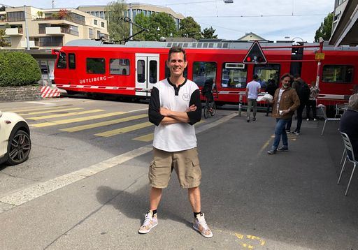 Lachender Mann mit verschränkten Armen vor Stadtbahn